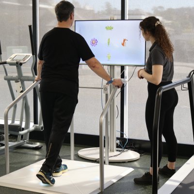 Man on exercise machine being watched by a woman